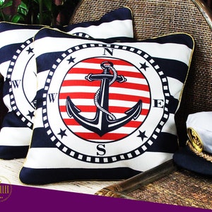 May include: Two decorative throw pillows with a nautical theme. The pillows are white and blue striped with a red, white, and blue anchor design in a compass circle. The compass points are N, E, S, and W.