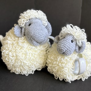 May include: Two crocheted sheep tea cozy sets. The larger sheep is white with a gray face and the smaller sheep is white with a gray face and a white teapot.