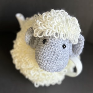 May include: A crocheted stuffed sheep toy with a white fluffy body and a gray face. The sheep has black eyes and a white nose.