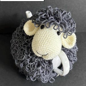 Peut inclure: Un dessous de thé en forme de mouton crocheté, gris et crème. Le dessous de thé est conçu pour s'adapter à une théière, avec le visage et les oreilles du mouton visibles. Le texte "PDF PATTERN" est affiché en haut.