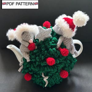Op de afbeelding: Een gehaakte theemuts in de vorm van een kerstboom met twee grijze muizen die rood-witte kerstmutsen dragen. De boom is versierd met kleine rode bollen en een zilveren ster. De tekst PDF PATTERN is zichtbaar in de linkerbovenhoek.