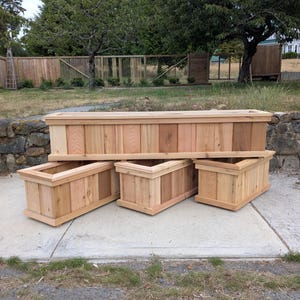May include: A set of four rectangular wooden planters constructed from natural cedar planks. The collection includes one long, wide planter positioned horizontally above three smaller, matching rectangular planters arranged in a row below it.