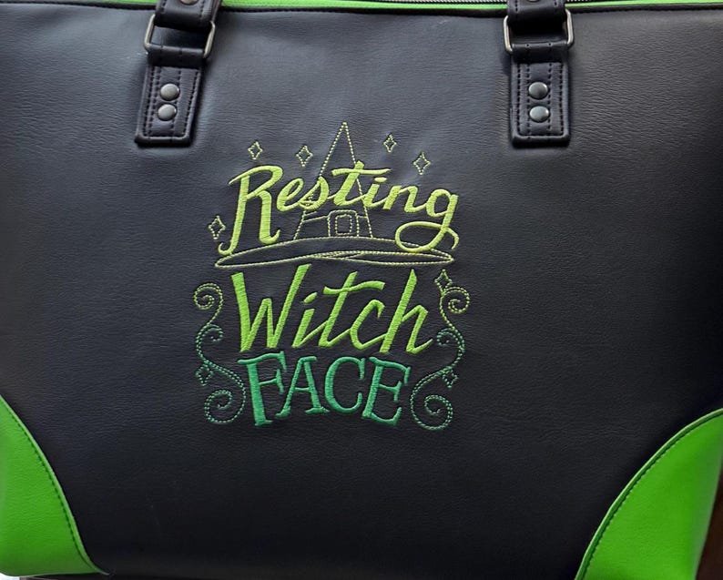 May include: Black tote bag with green accents and handles. The bag features the embroidered phrase "Resting Witch Face" in green and yellow, along with a witch hat design. The bottom corners are green.