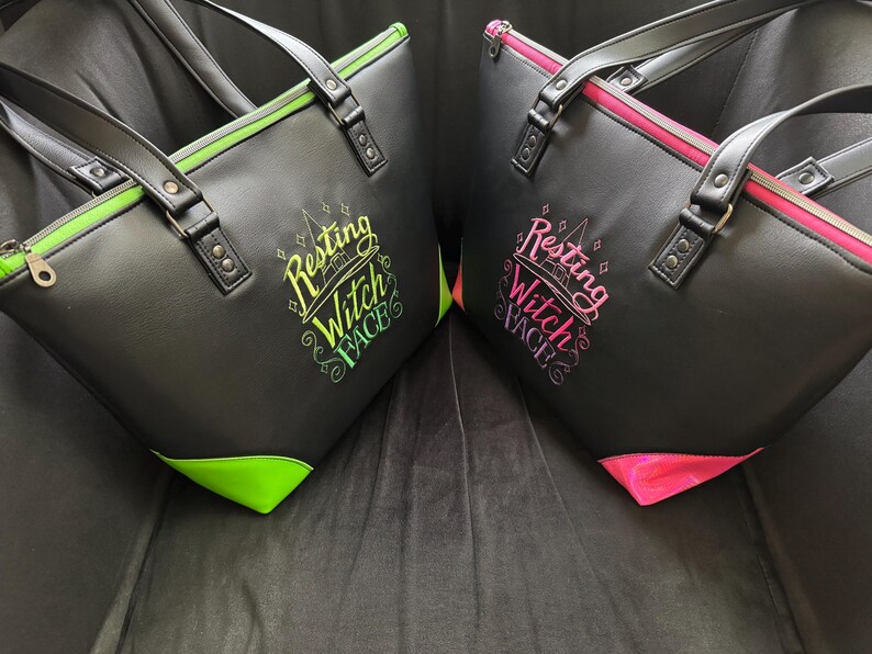 May include: Two black tote bags with the text "Resting Witch Face" in colorful lettering. One bag has green accents, the other pink. Both have black handles and zippers.