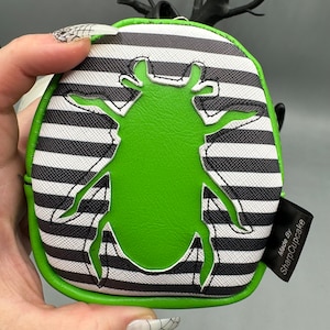 May include: A green beetle silhouette on a black and white striped fabric coin purse. The purse is made by SharpCupcake.
