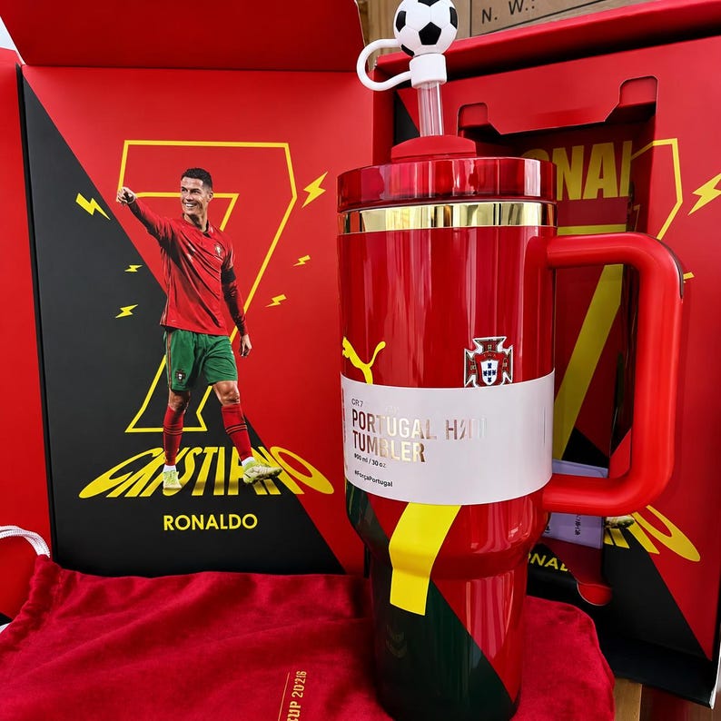 May include: A red and green tumbler with a handle, featuring a soccer ball topper on the straw and a white band labeled CR7 PORTUGAL TUMBLER 900 ml / 30 oz. The tumbler is displayed in a red box with a graphic of Cristiano Ronaldo and the number 7.