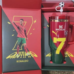 May include: A red and green Stanley tumbler featuring the number 7, a Puma logo, and the Portugal national team crest. The tumbler includes a straw with a soccer ball topper and is presented in a matching red and green box with an image of Cristiano Ronaldo.
