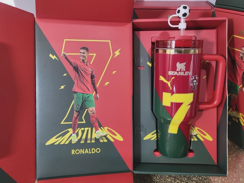 May include: A red and green Stanley tumbler featuring the number 7, a Puma logo, and the Portugal national team crest. The tumbler includes a straw with a soccer ball topper and is presented in a matching red and green box with an image of Cristiano Ronaldo.