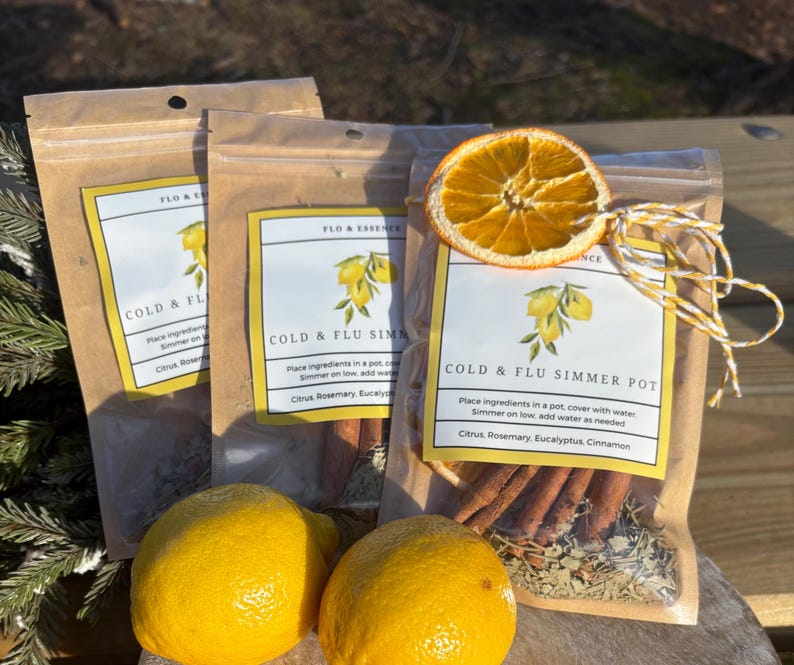 Op de afbeelding: Drie bruine papieren zakjes met een wit label waarop "Cold & Flu Simmer Pot" staat. Het label heeft een afbeelding van citroenen en de tekst "Place ingredients in a pot, cover with water. Simmer on low, add water as needed. Citrus, Rosemary, Eucalyptus, Cinnamon". De zakjes bevatten kaneelstokjes, gedroogde sinaasappelschijfjes en andere ingredi&euml;nten.