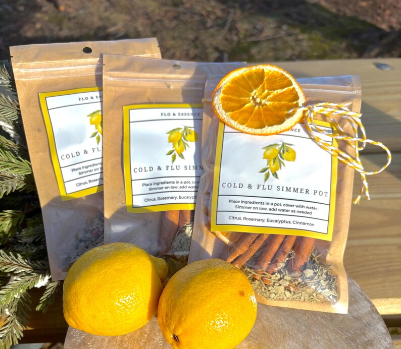 Op de afbeelding: Drie bruine papieren zakjes met witte etiketten waarop "Cold & Flu Simmer Pot" staat. De zakjes bevatten gedroogde citrusvruchten, kaneelstokjes, rozemarijn en eucalyptus. De zakjes zijn vastgebonden met touw en een gedroogde sinaasappelschijf.