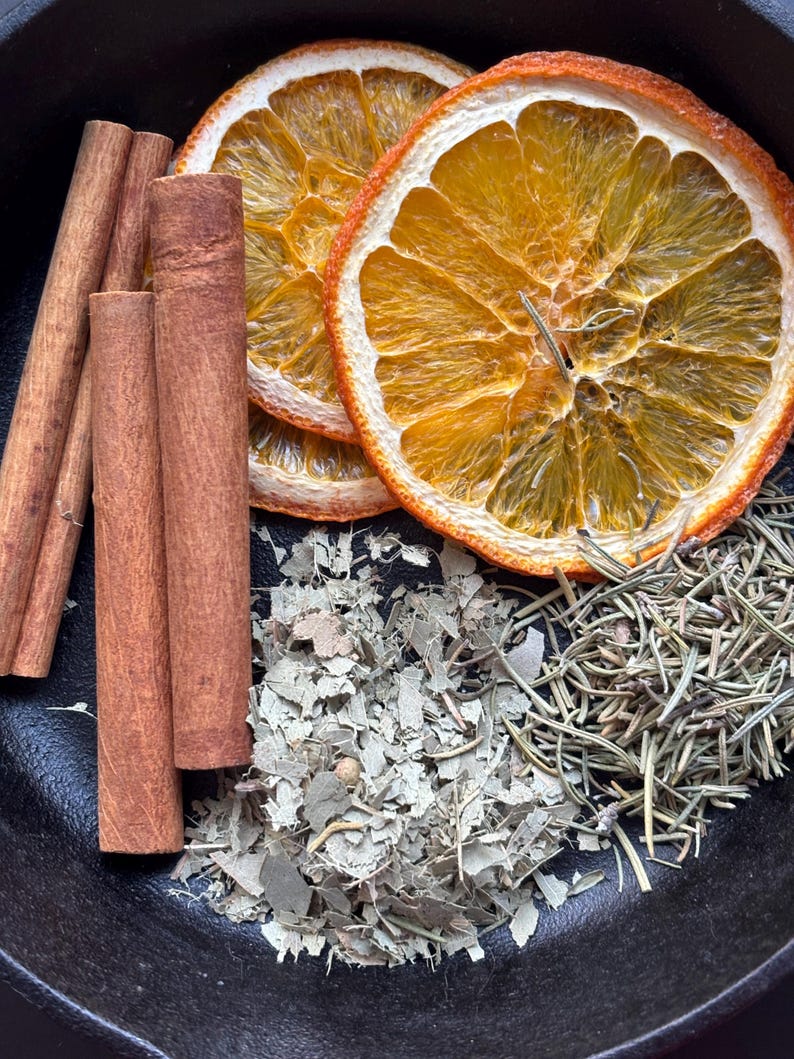 Op de afbeelding: Gedroogde sinaasappelschijfjes, kaneelstokjes, eucalyptusbladeren en rozemarijntakjes in een zwarte gietijzeren pan. Deze ingredi&euml;nten worden vaak gebruikt voor potpourri of om te sudderen op het fornuis voor een natuurlijke geur in huis.