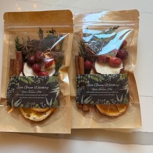 Könnte beinhalten: Zwei transparente Beutel gefüllt mit getrockneten Früchten, Gewürzen und Kräutern. Jeder Beutel enthält Zimtstangen, Sternanis, getrocknete Orangenscheiben und Preiselbeeren. Die Beutel haben eine braune Papierrückseite und ein Etikett mit der Aufschrift "Ever Green Witchery Yule Summer Pie."