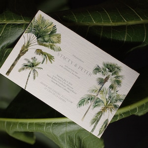 May include: A wedding invitation with a tropical theme. The invitation features a watercolor illustration of palm trees and the text "Stacy & Peter" in a simple, elegant font. The invitation is set against a white background.