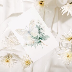 Pu&ograve; includere: Una farfalla bianca con foglie verdi e fiori bianchi su uno sfondo bianco. La farfalla &egrave; dipinta ad acquerello e ha un aspetto delicato ed etereo.