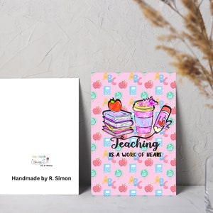 May include: A pink card with a colorful illustration of books, a coffee cup, and a pencil. The text "Teaching is a work of heart" is written in black on the card. The background is a pink pattern of apples, ABCs, and other school-related items.
