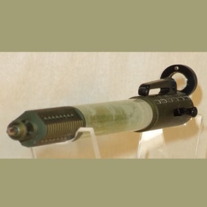 May include: A green and black metal object with a clear tube in the middle. The tube is filled with a green substance. The object has a handle and a ring on the end.