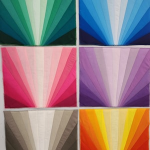 May include: Six fabric squares with a sunburst design in different colors. The colors are green, blue, pink, purple, gray, and orange.