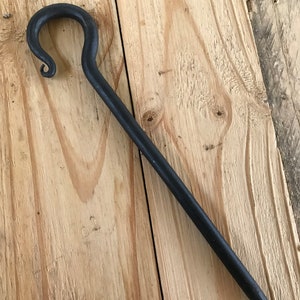 May include: A black metal hook with a curved handle. The hook is made of forged metal and has a rustic finish.