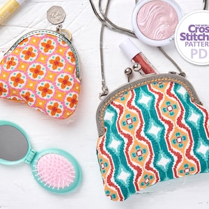 May include: Two small, colourful, cross-stitch purses with metal clasps. The purse on the left has a geometric pattern in shades of orange, pink, and yellow. The purse on the right has a geometric pattern in shades of red, green, and blue. The purses are on a white surface with other items, including a small mirror and a makeup brush.