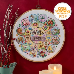 K&ouml;nnte beinhalten: Ein Kreuzstichmuster in einem Holzrahmen zeigt ein farbenfrohes Design mit dem Text "Hello November". Das Design umfasst saisonale Bilder wie einen Schneemann, Blumen und einen Bienenstock. Der Text "The World of Cross Stitching Patterns PDF" ist ebenfalls sichtbar.