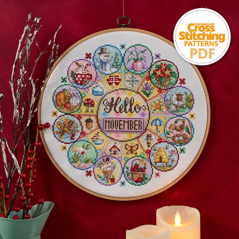 K&ouml;nnte beinhalten: Ein Kreuzstichmuster in einem Holzrahmen zeigt ein farbenfrohes Design mit dem Text "Hello November". Das Design umfasst saisonale Bilder wie einen Schneemann, Blumen und einen Bienenstock. Der Text "The World of Cross Stitching Patterns PDF" ist ebenfalls sichtbar.