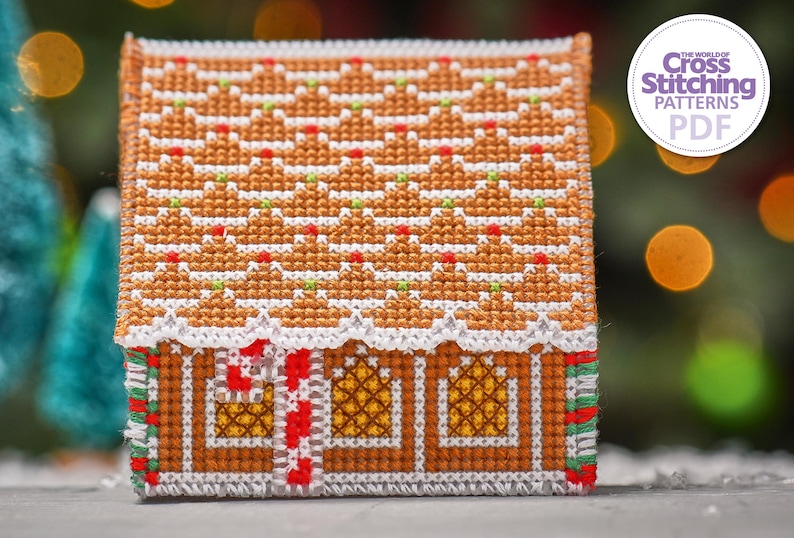 May include: A cross stitch pattern of a gingerbread house with a white roof, red candy canes, and yellow windows. The pattern is on a white background with the text "The World of Cross Stitching Patterns PDF" in a purple circle.