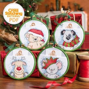 May include: Four cross-stitch Christmas ornaments with cartoon animal designs: a bear in a Santa hat, a dog with a scarf, a reindeer, and a mouse with a crown. Each ornament is round, framed in green, and has a small pocket. The text "THE WORLD OF Cross Stitching PATTERNS PDF" is in the upper left.