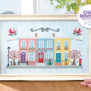 May include: A cross stitch pattern of a row of colourful houses with red doors, windows, and flower boxes. The houses are decorated with bunting and trees. The pattern is framed in a white frame and is titled "The World of Cross Stitching Patterns PDF".