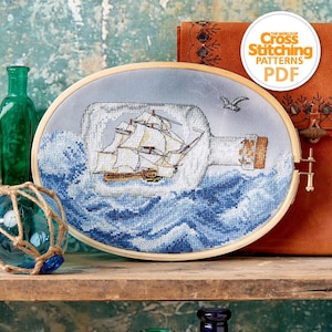 Peut inclure: Une broderie au point de croix ovale représentant un navire dans une bouteille, sur fond de vagues bleues et de ciel bleu clair. La broderie est encadrée dans un cercle en bois. Une mouette vole au-dessus du navire. Le texte "The World of Cross Stitching Patterns PDF" est en haut à droite.