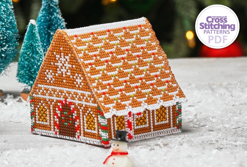 May include: A cross stitch pattern of a gingerbread house with white icing, candy canes, and a green wreath. The house is on a white background with a small snowman in the foreground. The text "The World of Cross Stitching Patterns PDF" is in the upper right corner of the image.