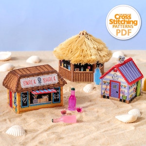 May include: Three cross-stitch beach hut models with thatched roofs, set on sand with seashells and miniature pink bottles. One hut has "SNACK SHACK" text, another has a surfboard, and the third has an anchor design. A "Cross Stitch Patterns PDF" logo is in the corner.