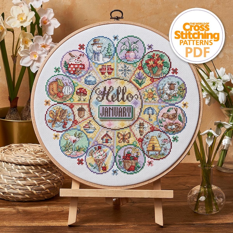 K&ouml;nnte beinhalten: Ein Kreuzstichmuster in einem Holzrahmen, mit einem kreisf&ouml;rmigen Design mit saisonalen Illustrationen. In der Mitte steht "Hello January". Das Design enth&auml;lt Bilder von einem Schneemann, Blumen und anderen saisonalen Elementen. Der Text "The World of Cross Stitching Patterns PDF" befindet sich oben rechts.