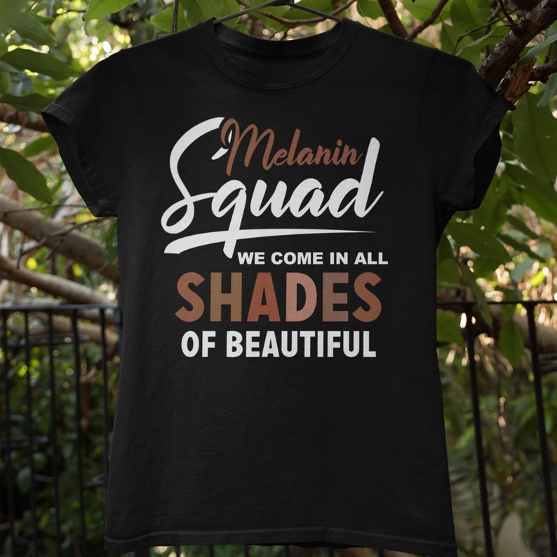 May include: Black t-shirt with white text that reads "Melanin Squad We Come In All Shades Of Beautiful". The text "Shades" is in rainbow colors.