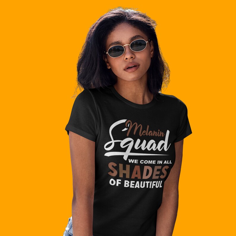 May include: A black t-shirt with the text "Melanin Squad We Come In All Shades Of Beautiful" in white and brown lettering.