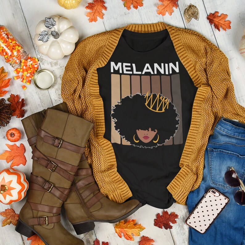 May include: Black t-shirt with a graphic of a woman with an afro wearing a crown. The graphic is surrounded by a rainbow of skin tones. The text "MELANIN" is above the graphic.