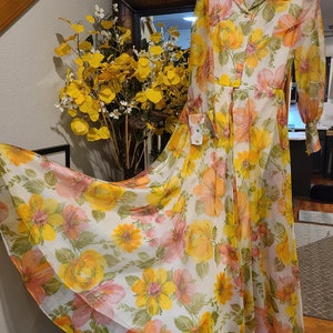 May include: A long-sleeved, white maxi dress with a floral print in shades of yellow, orange, and pink. The dress has a collared neckline, button-up front, and long sleeves with buttoned cuffs.
