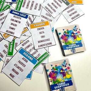 Può includere: Primo piano di un gioco chiamato "Taboo Scientifico" con carte colorate che presentano termini scientifici in italiano. Le carte sono sparse su una superficie bianca.