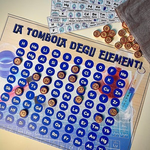 Può includere: Un gioco da tavolo chiamato "IA TOMBOLA DEGU ELEMENTI" con un design della tavola periodica. Include cerchi blu con simboli degli elementi, gettoni di legno con numeri e carte degli elementi. Un divertente gioco educativo.