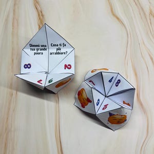 Può includere: Due indovinelli di carta bianca, anche conosciuti come cootie catchers, con linee nere e numeri colorati. Un indovinello ha il testo "Dimmi una tua grande paura" e "Cosa ti fa più arrabbiare?" su di esso. L'altro indovinello ha i numeri 1, 2, 4, 6, 7, 8 e 9 su di esso.