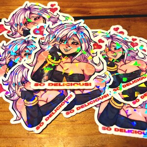 May include: Holographic stickers depicting a smiling anime character with pink hair and a black outfit. The stickers have a heart and the text "SO DELICIOUS!". The stickers are on a wooden surface.