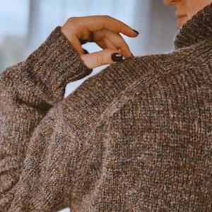 Puede incluir: Un suéter de punto marrón con cuello alto. El suéter está hecho de un material suave y peludo.