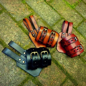 May include: Three leather wrist cuffs with metal buckles. The cuffs are in brown, black, and red leather.