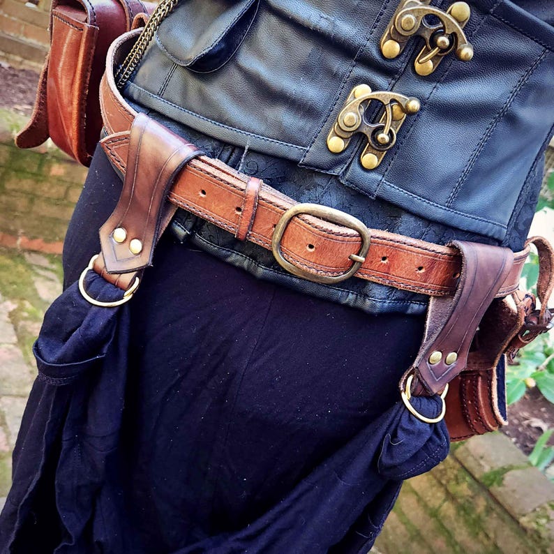 May include: A brown leather belt with two leather pouches attached. The belt has a brass buckle and the pouches have brass rings.