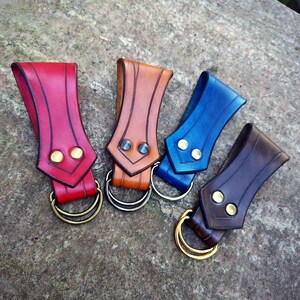 May include: Four leather belt loops with metal rings. The loops are in red, brown, blue, and dark brown.