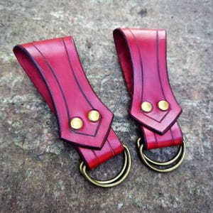 May include: Two red leather sword belt loops with brass rings and rivets.