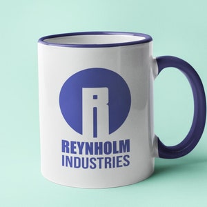 Op de afbeelding: Een witte keramische mok met een blauw handvat en rand. De mok toont de tekst "REYNHOLM INDUSTRIES" in blauw, samen met een blauw cirkelvormig logo met de letter "R". De mok staat tegen een lichtblauwe achtergrond.