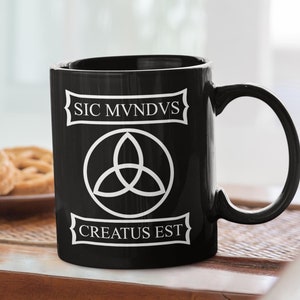 May include: Black ceramic coffee mug with a white graphic of a triquetra symbol and the text "SIC MVNDVS CREATUS EST".