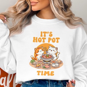 May include: White sweatshirt featuring a graphic of two cats enjoying a hot pot meal. The text on the sweatshirt reads "It's Hot Pot Time".