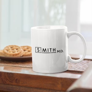 May include: White ceramic mug with a black square and the text "SMITH M.D." printed on the front.