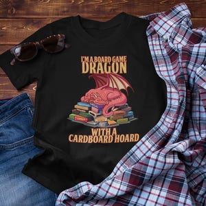 Camiseta Dragão de Jogo de Tabuleiro. Draon com um Acervo de Papelão. Camiseta amante de jogos de tabuleiro.